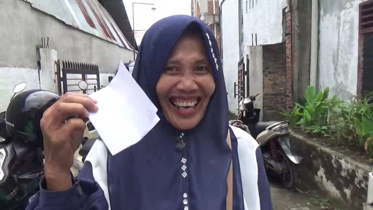 Sulia, warga Marelan, menunjukkan bingkisan dan amplop yang diterimanya usai menghadiri Sosperda Roma Uli Silalahi. Ia mengaku senang mendapatkan informasi seputar perumahan kumuh serta menerima bingkisan berupa botol sirup dan amplop berisi uang, Minggu, 23 Maret 2025, Zeze Futsal, Jalan Marelan Raya, Gang Sepakat, Kelurahan Rengas Pulau, Kecamatan Medan Marelan, Kota Medan (Foto: Dok. pelitaharian.id).
